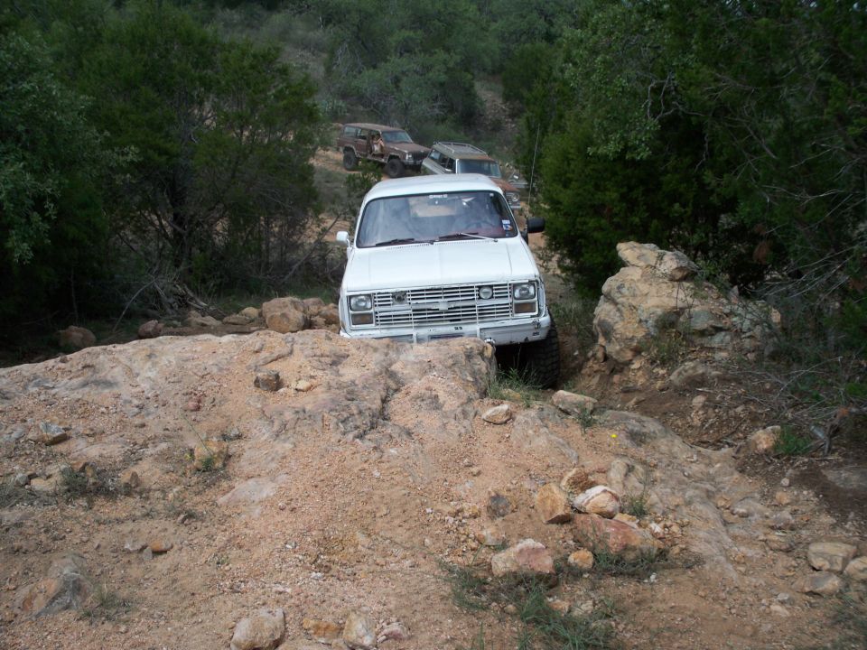 White Chevrolet pickup truck navigating rocky terrain, with other SUVs behind
