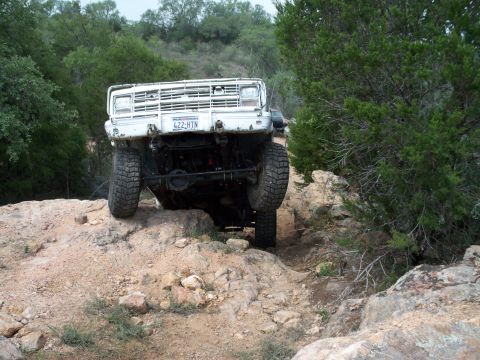 1996 Ford Bronco - A white off-road vehicle tackles a challenging rocky path, its front grille and license plate visible.
