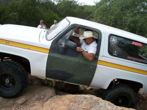 1996 Ford Bronco - A man in a cowboy hat drives a modified SUV over a rocky terrain.