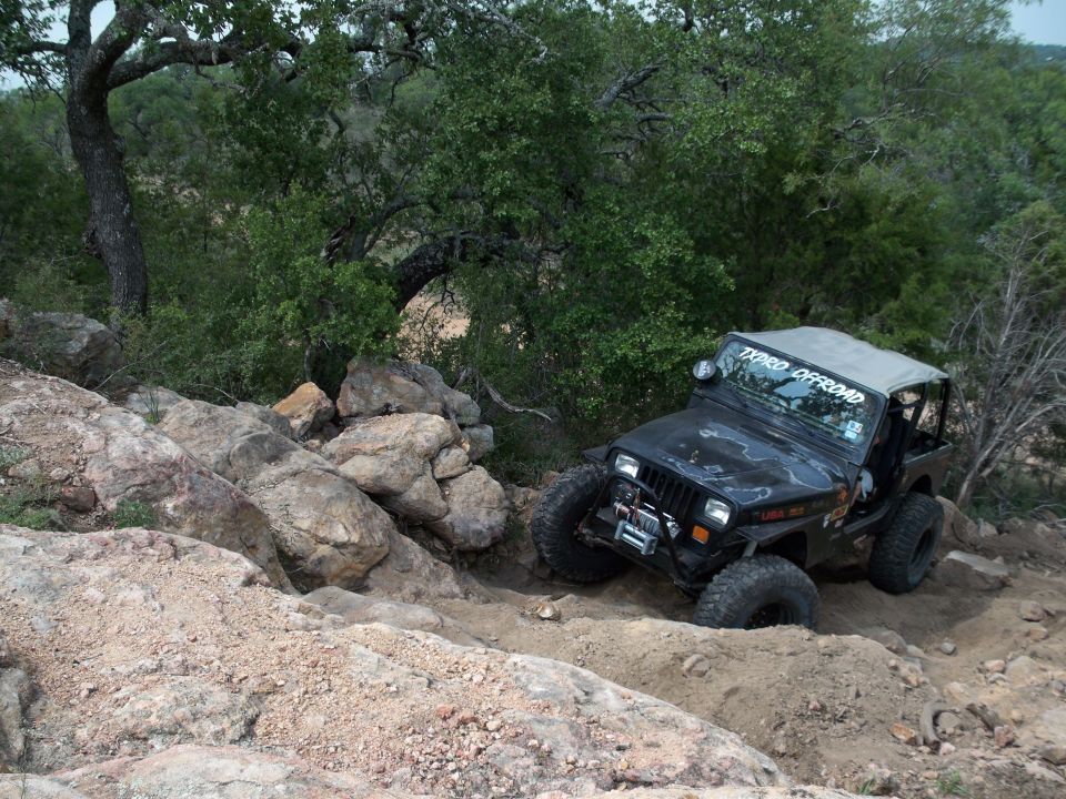 Black Jeep Wrangler with a soft top navigating a rocky, off-road trail