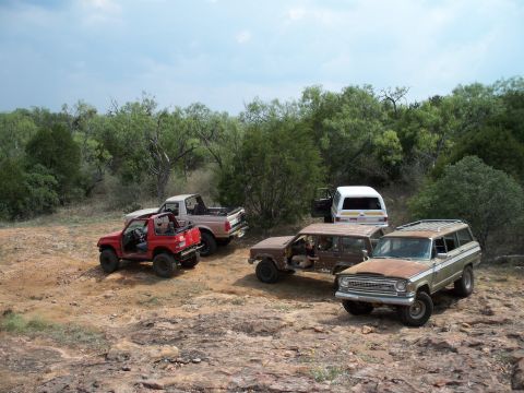 1996 Ford Bronco - Several off-road vehicles are parked on a dirt and rocky terrain under a cloudy sky.