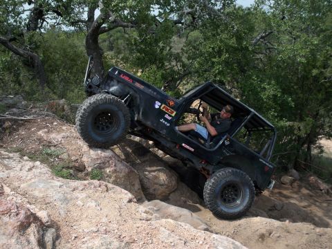 1996 Ford Bronco - A driver navigates a heavily modified Jeep Wrangler over a rocky incline on an off-road trail.