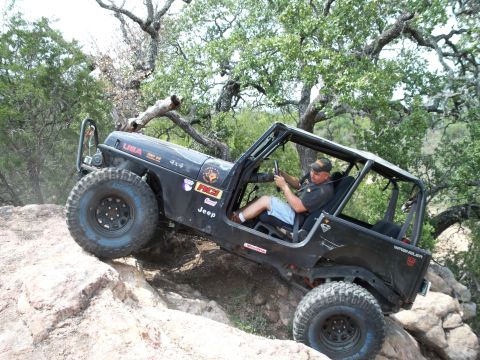 1996 Ford Bronco - A black Jeep Wrangler navigates a rocky incline with a driver behind the wheel.