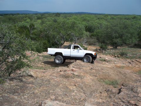 1996 Ford Bronco - A white pickup truck navigates a rocky terrain with a dense forest in the background.