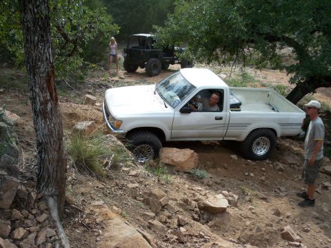 1996 Ford Bronco - A white pickup truck navigates a challenging off-road terrain with a driver and another vehicle in the background.