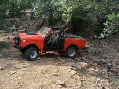 1996 Ford Bronco - Off-road vehicle navigating a challenging rocky path with trees overhead.