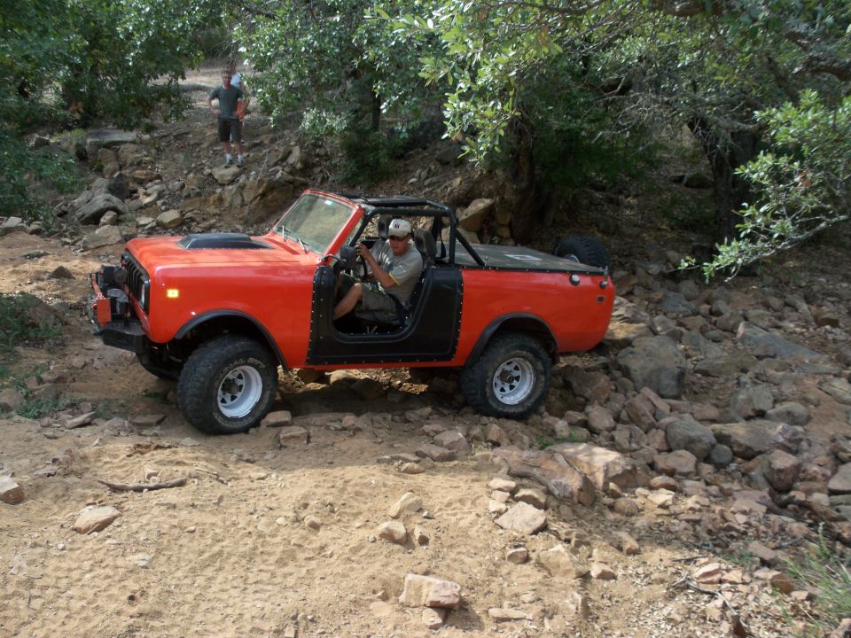 Orange off-road vehicle with black doors and roll cage driving on a rocky trail