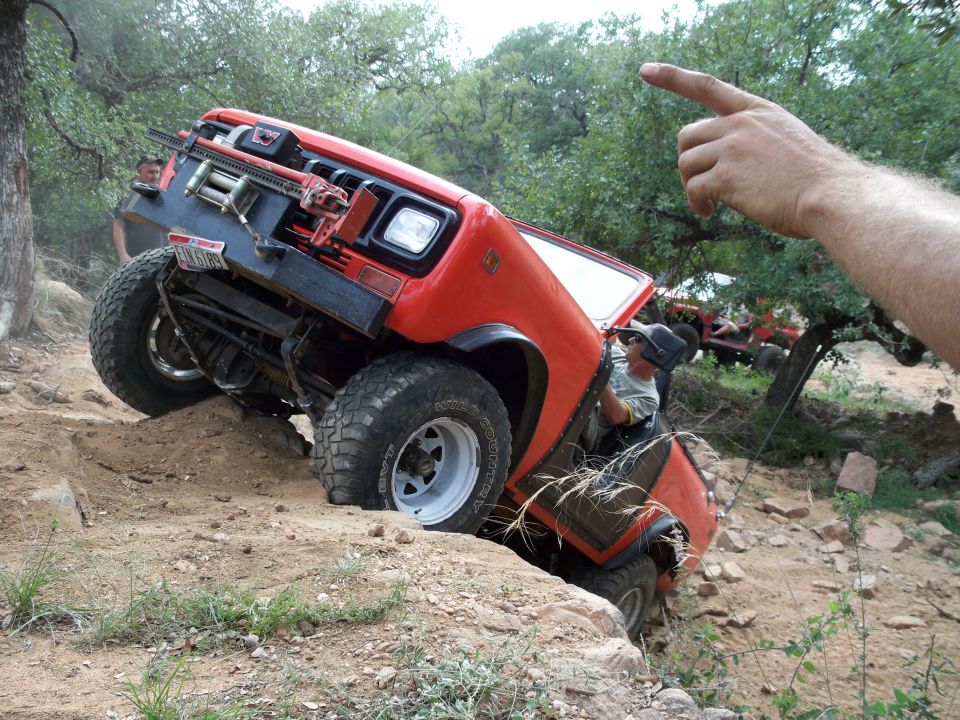 Red off-road vehicle climbing a dirt hill with a winch and jack mounted