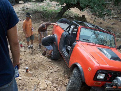 1996 Ford Bronco - People gathered around an orange off-road vehicle that appears to be stuck in the dirt.