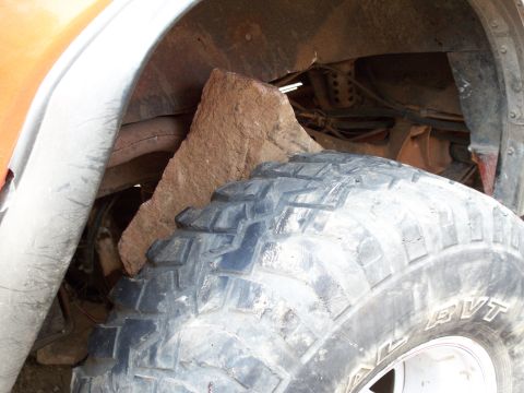 1996 Ford Bronco - A large rock is lodged in the wheel well of an off-road vehicle, just behind the tire.