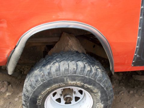 1996 Ford Bronco - A rock is lodged in the wheel well of an orange SUV, pressing against the tire.