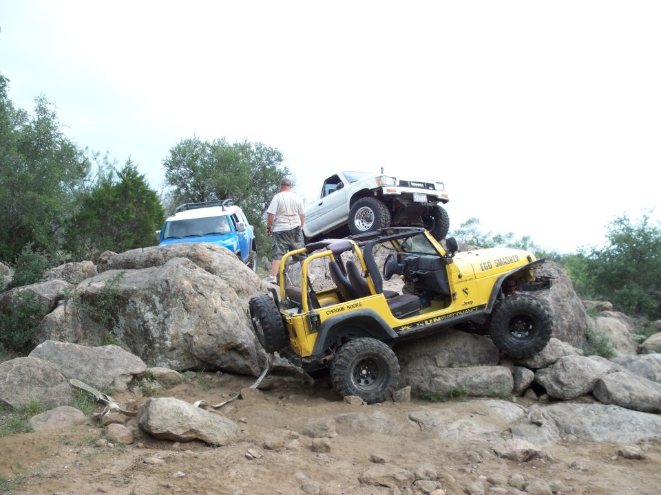 Yellow Jeep Wrangler and white Toyota pickup truck navigating rocky terrain