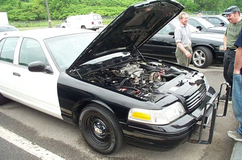 1991 Ford LTD Crown Victoria - A black and white Ford Crown Victoria with its hood open, revealing the engine, is parked next to other vehicles.