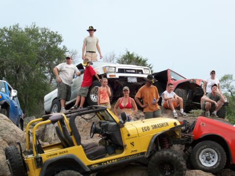 1996 Ford Bronco - A group poses with their off-road vehicles, including a yellow Jeep, a red Jeep, and a white Toyota truck, on a rocky terrain.