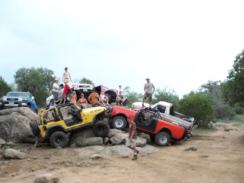 1996 Ford Bronco - A group of off-road vehicles are positioned on rocks, with several people standing and sitting around them.