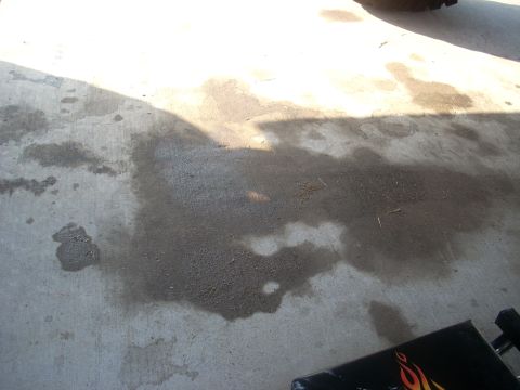 1992 Ford Bronco - Oil stains on a concrete surface, possibly indicating a vehicle leak, with a partial view of a black object and text.
