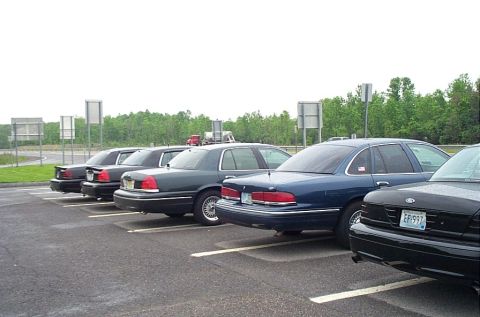 1991 Ford LTD Crown Victoria - Multiple Ford Crown Victoria police cars are parked in a lot under an overcast sky.