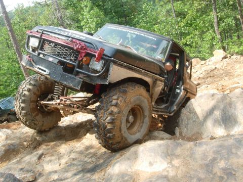 1995 Ford Bronco - This heavily modified SUV navigates a challenging rocky terrain on an off-road trail.