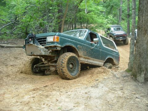 1995 Ford Bronco - Off-road vehicles navigate a muddy trail through a wooded area.