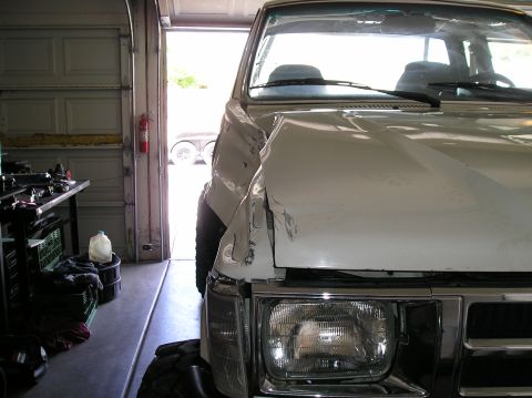 1986 Toyota Hilux - Front view of a damaged 1986 Toyota Hilux in a garage, showing dented body panels.