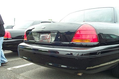 1991 Ford LTD Crown Victoria - Two black Ford Crown Victorias are parked side-by-side, showing their rear ends and license plates.