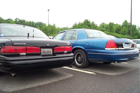 1991 Ford LTD Crown Victoria - Two Ford Crown Victorias are parked side-by-side in a lot, one black and one blue.