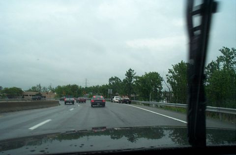1991 Ford LTD Crown Victoria - A view from inside a vehicle on a highway, with several other cars visible on the wet road under an overcast sky.