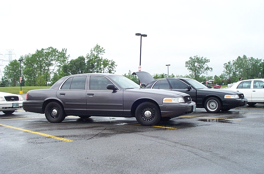 Gray Ford Crown Victoria parked next to a black one and a white one. Hood of the black car is open