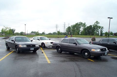 1991 Ford LTD Crown Victoria - Four sedans are parked in a wet lot under an overcast sky.