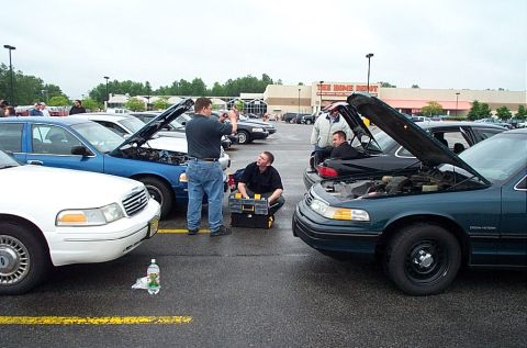 1991 Ford LTD Crown Victoria - Mechanics attend to a 1991 Ford Crown Victoria LTD in a parking lot, with other vehicles also present.