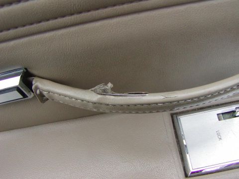 1991 Ford LTD Crown Victoria - Close-up of a worn car interior door panel showing damage to the armrest and a lock mechanism.