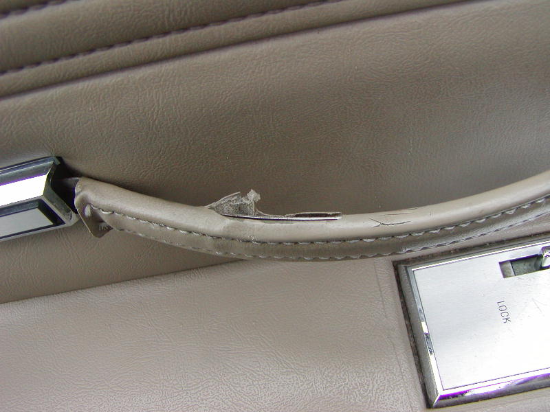 Tan leather car door panel with chrome trim and a torn armrest