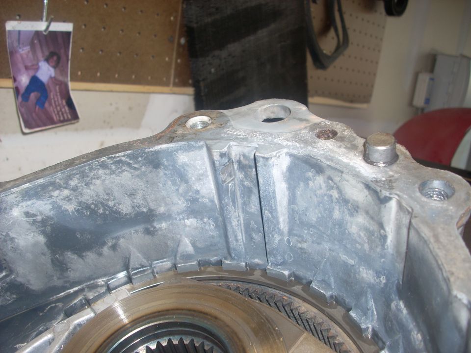 Close-up of a transfer case housing with internal gears visible. A small photo is clipped to a pegboard in the background