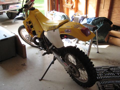 1993 Suzuki RMX250 - A yellow dirt bike is parked indoors, showing its side profile and Suzuki branding on the seat.