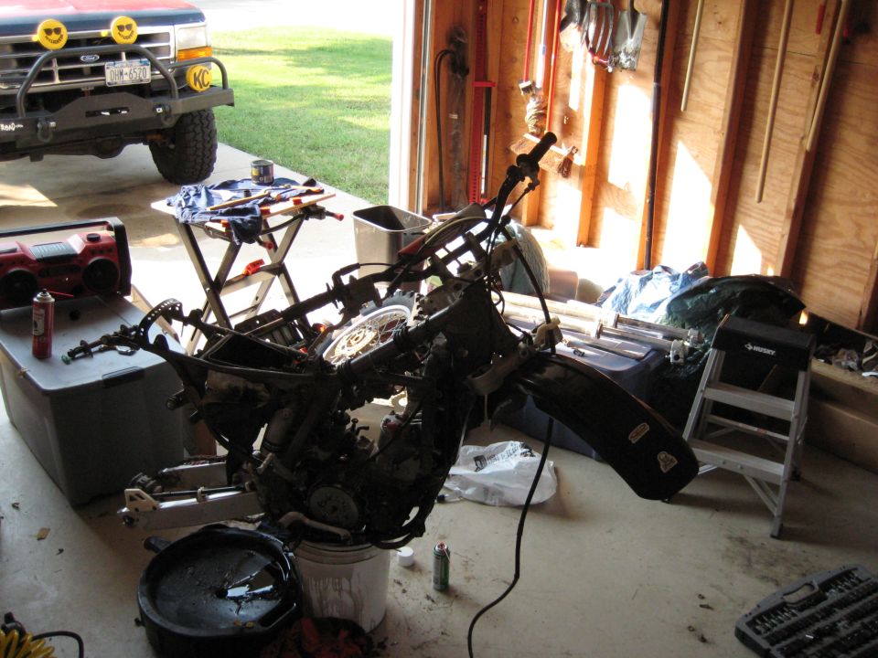Disassembled dirt bike frame and engine on garage floor during teardown