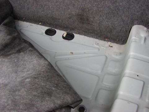 1991 Ford LTD Crown Victoria - The underside of the rear passenger carpet is visible, revealing the car's floor pan and two rubber grommets.