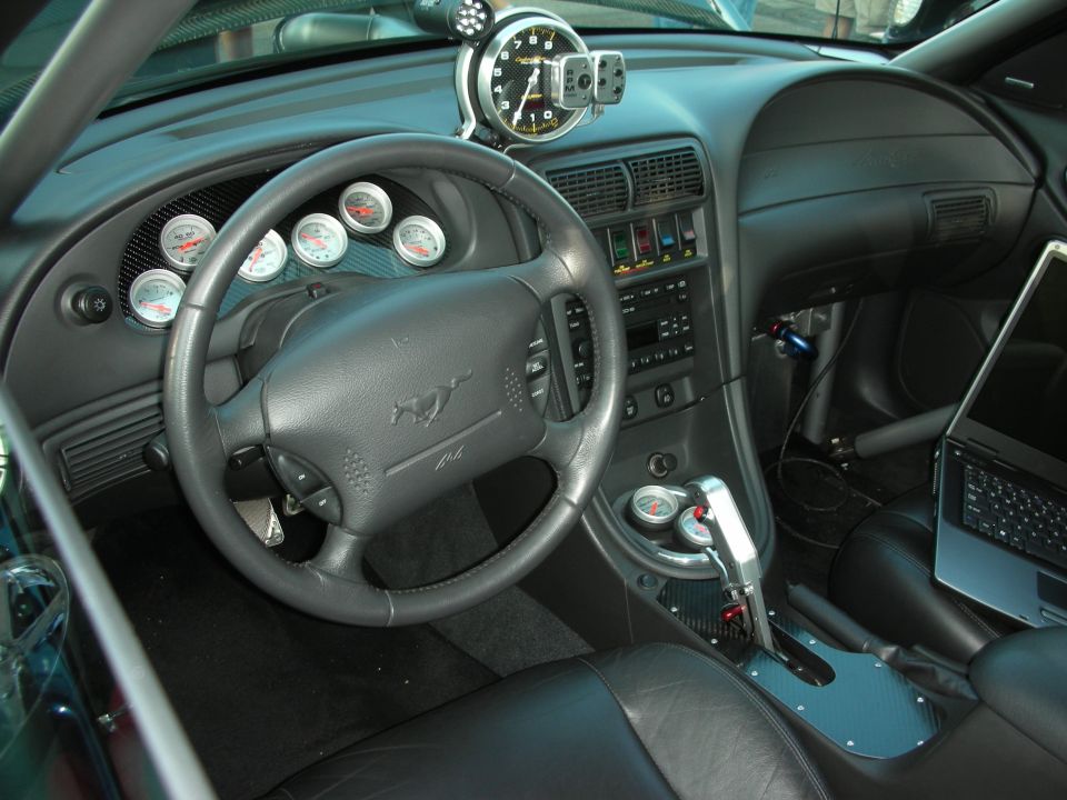 Interior view of a modified car with a tachometer, gauges, and a laptop on the passenger seat