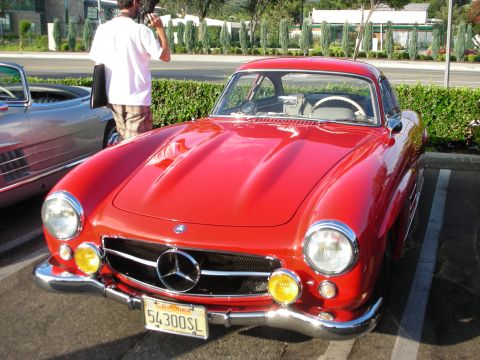 1998 Ford Crown Victoria - A red Mercedes-Benz 300SL coupe is parked next to another classic car, its distinctive gullwing doors and yellow fog lights.