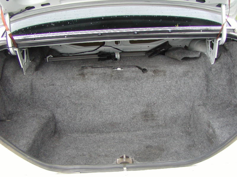 Empty gray carpeted sedan trunk with factory jack and handle mounted on front wall