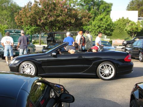 1998 Ford Crown Victoria - A group of people stand around several cars at an outdoor gathering.