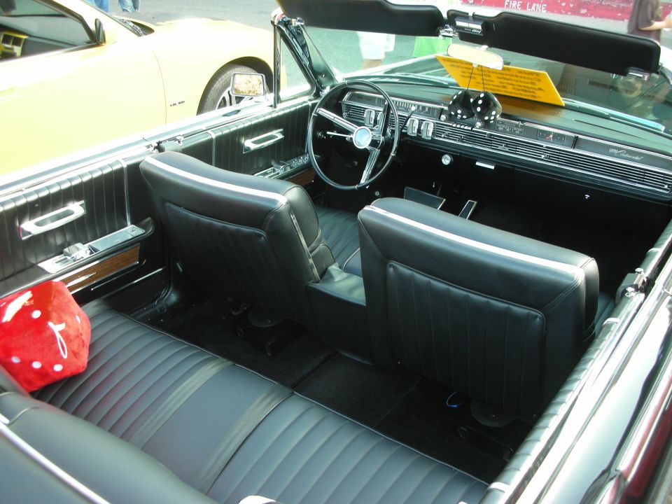 Interior of a black convertible with a yellow car visible outside. Dice hanging from rearview mirror