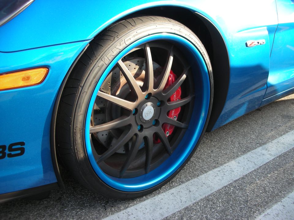 Close-up of a blue sports car's front wheel with a blue lip, red brake caliper, and a Z06 badge visible on the fender