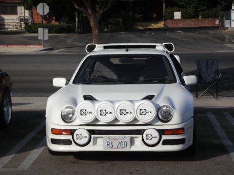 1998 Ford Crown Victoria - A white Ford RS200 is parked in a lot, equipped with multiple Cibie spotlights and a custom license plate.