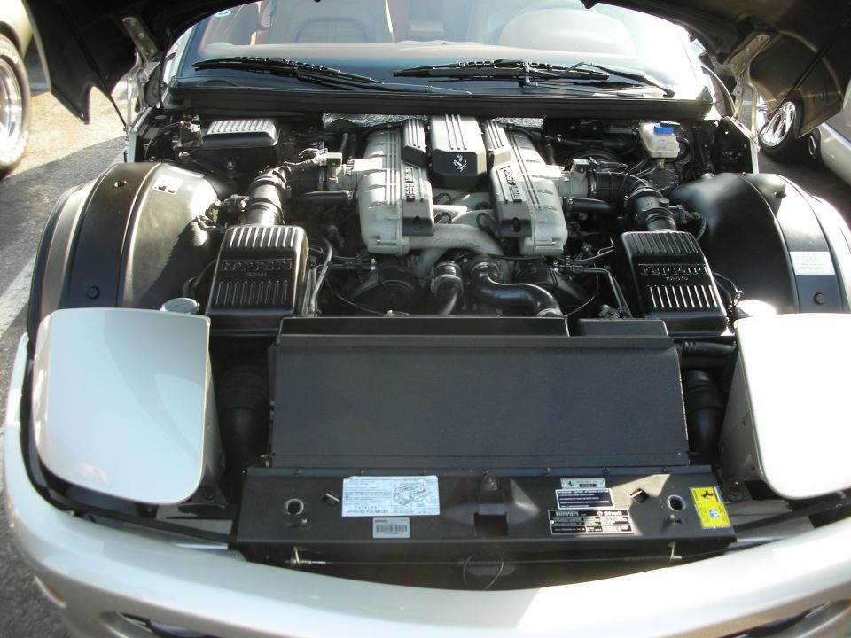 Ferrari V8 engine with twin camshaft covers, air intake boxes, and front headlights visible