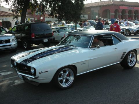 1998 Ford Crown Victoria - A white 1969 Chevrolet Camaro Z/28 is parked at an outdoor event with other vehicles and people around.