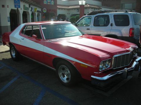 1998 Ford Crown Victoria - A red and white 1975 Ford Gran Torino is parked in a lot next to a silver SUV.