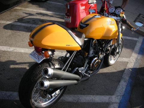 1998 Ford Crown Victoria - Yellow Ducati motorcycle parked in a lot, showing its rear section and dual exhaust.