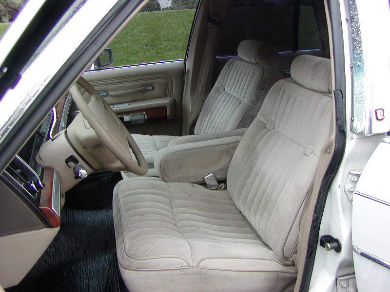 Tan velour interior of a 1990s sedan, showing front seats, dashboard, and steering wheel