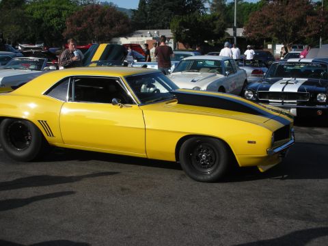 1998 Ford Crown Victoria - A yellow 1969 Chevrolet Camaro with black racing stripes is parked at an outdoor car meet.