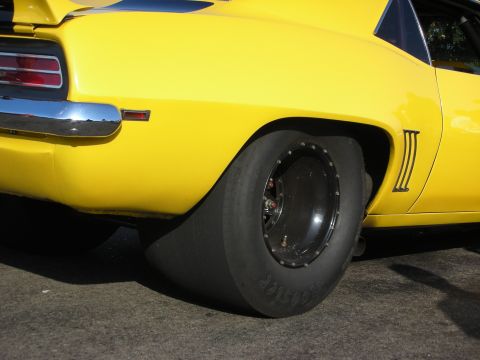 1998 Ford Crown Victoria - Close-up of a yellow muscle car's rear quarter panel, a large drag slick tire and chrome bumper details.